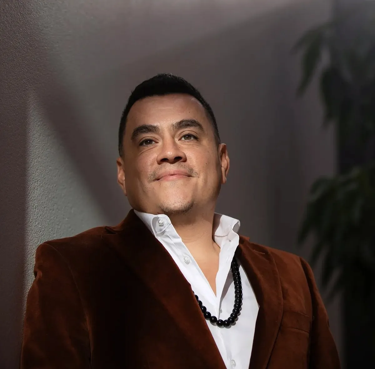 Alfredo Reyes in a rust velvet jacket and white shirt, smiling in warm afternoon light